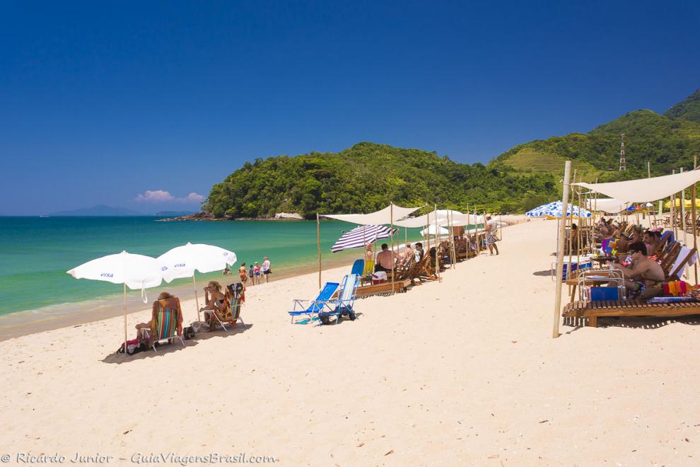 Imagem de turistas nas areias em baixo do guarda sol se protegendo-Praia de Prumirim.